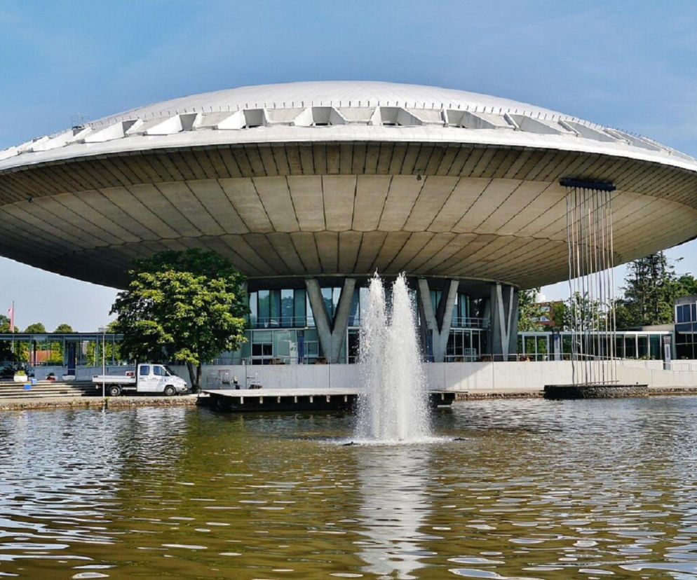 Budynek Evoluon w Eindhoven o kształcie spodka stoi nad wodą z fontanną. O architekturze obiektu przeczytasz na Architektura.