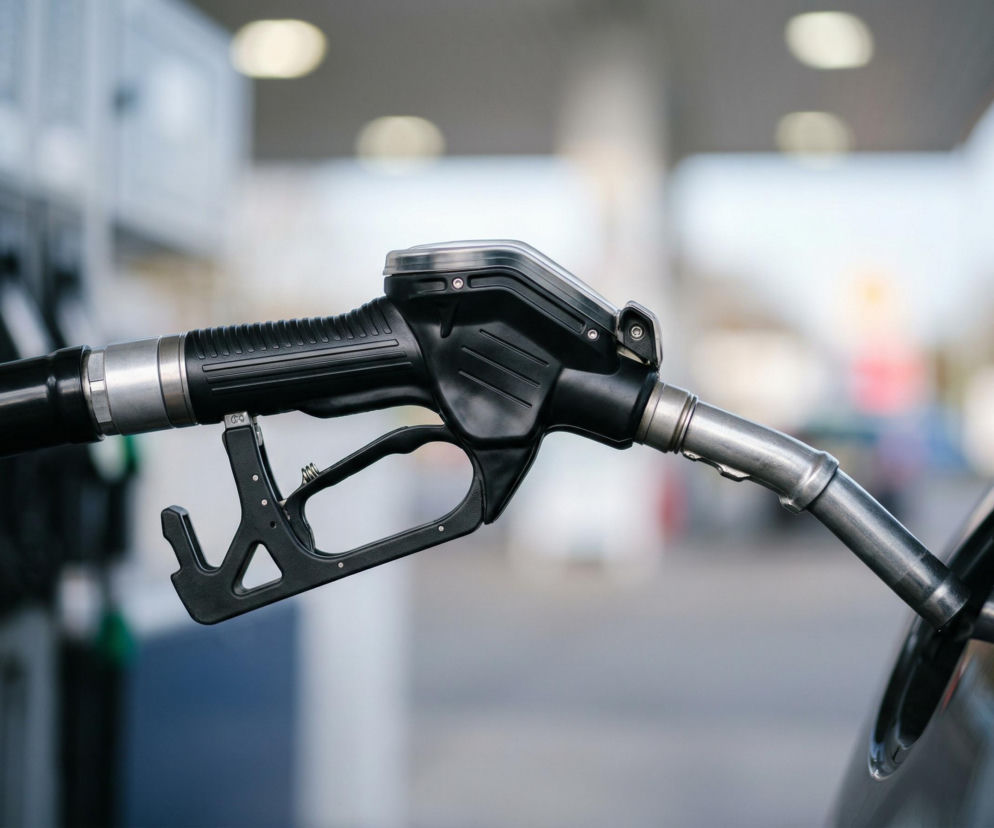 Czarny pistolet do tankowania paliwa włożony do wlewu paliwa samochodu, symbolizujący aktualne informacje o hurtowych cenach paliw oraz szanse na niższe koszty tankowania, dostępne na portalu Super Biznes.