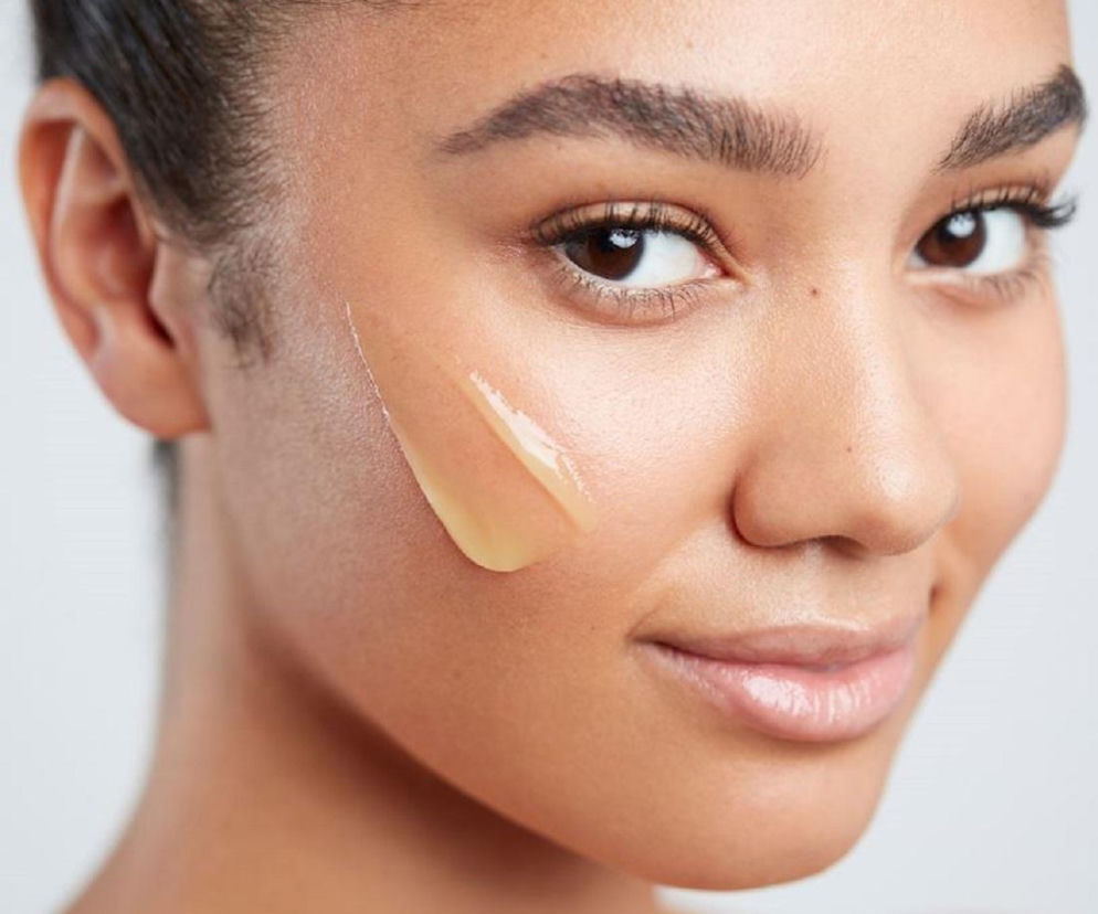Młoda kobieta z nałożoną smugą balsamu na policzku. O jesiennych trendach beauty przeczytasz na SE.