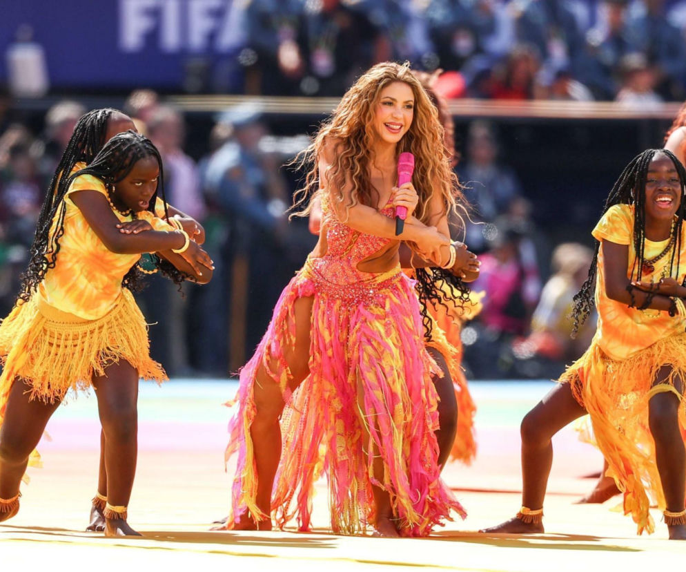 Uśmiechnięta Shakira śpiewa do różowego mikrofonu w otoczeniu tancerek. O krytyce show na mundialu przeczytasz w Eska.