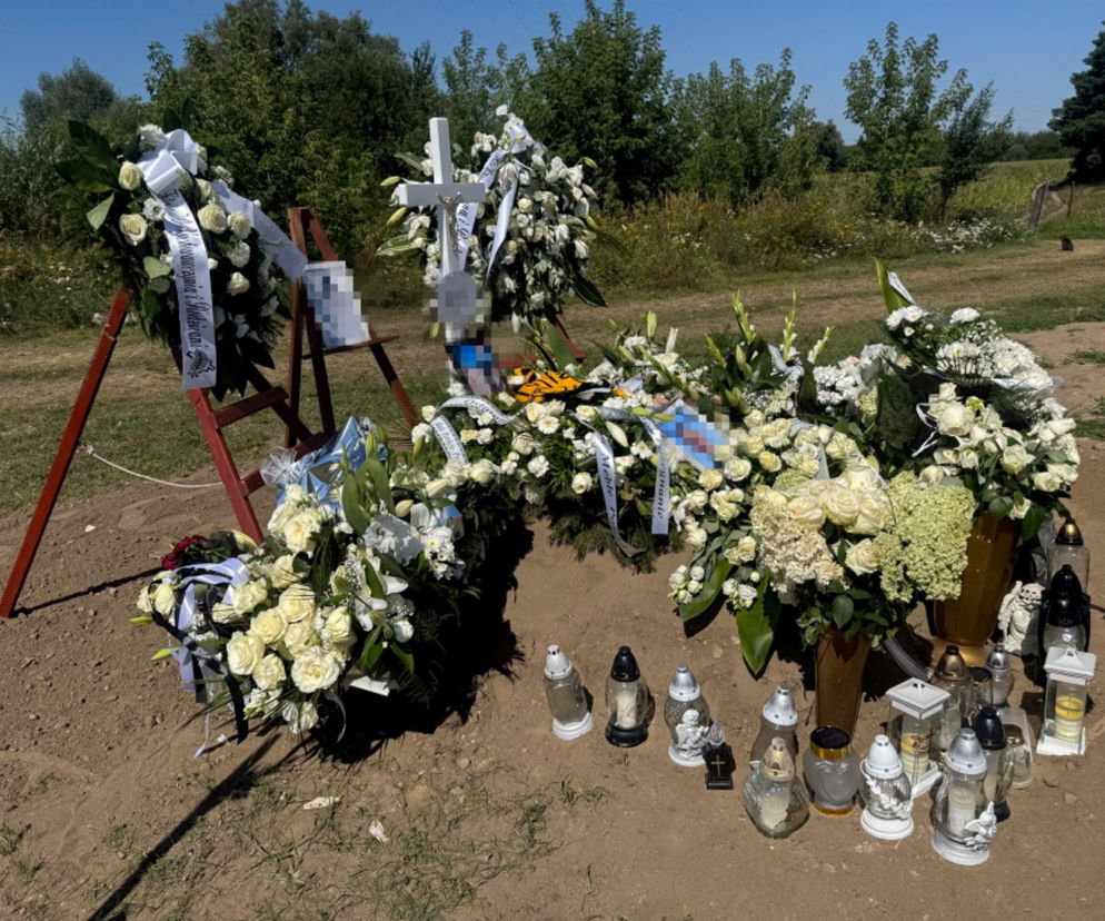 Grób nastolatka z licznymi białymi kwiatami, zniczami i zdjęciem chłopca. O tragedii przeczytasz na Eska Poznań.