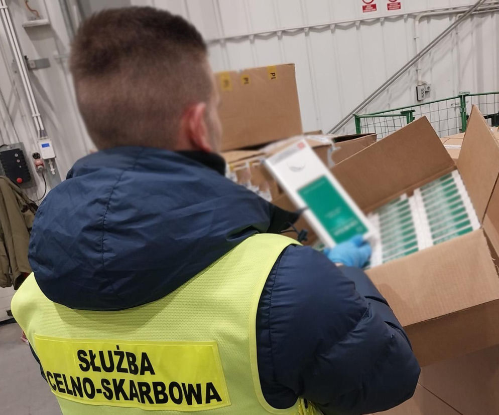 Funkcjonariusz Służby Celno-Skarbowej w kamizelce ochronnej, kontrolujący zawartość kartonowych paczek z nielegalnymi papierosami bez polskich znaków akcyzy, przemycanymi z Dubaju. Więcej o udaremnionym przemycie na portalu Super Biznes.