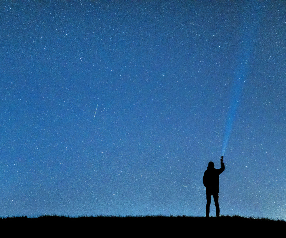 Sylwetka osoby na wzgórzu pod rozgwieżdżonym niebem z meteorem. O Nocy Perseidów 2026 przeczytasz na Eska Kielce.