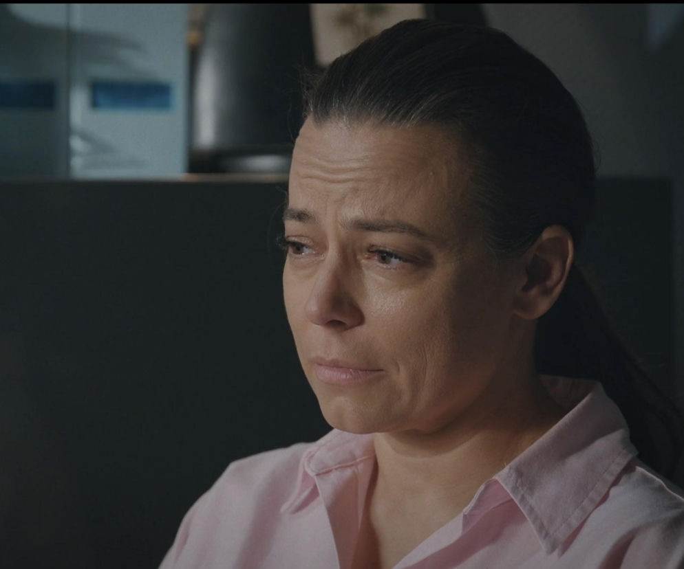 Zbliżenie na twarz Magdy Budzyńskiej (Anna Mucha) z serialu M jak miłość, widać na niej smutek i zmęczenie, z oczu spływają łzy. Twarz bohaterki jest poważna, a jej włosy są związane w niski kucyk. Ubrana jest w różową koszulę. Więcej o losach Magdy przeczytasz na Super Seriale.