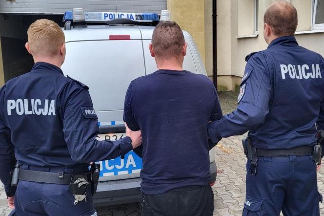 Dwaj policjanci prowadzą zatrzymanego mężczyznę do radiowozu. O areszcie dla recydywisty przeczytasz na Radioplus.