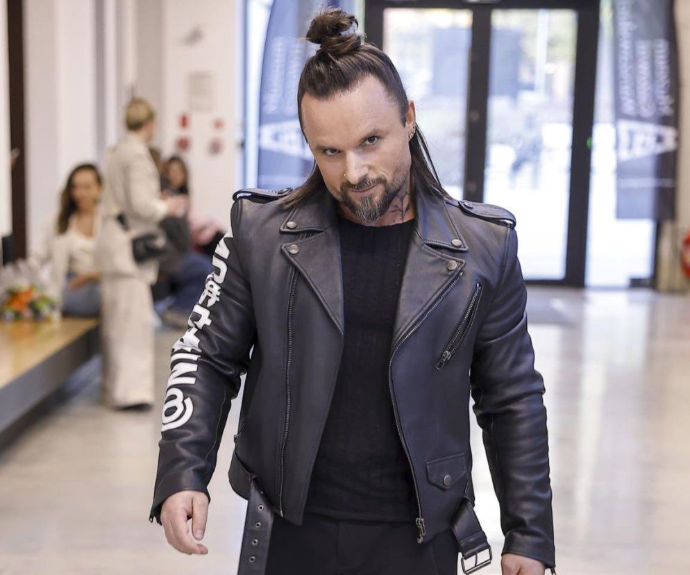 Daniel Qczaj Kuczaj, znany trener fitness i motywator, ubrany w czarną skórzaną kurtkę z naszywkami na rękawach oraz ciemną koszulkę, z włosami upiętymi w koka i brodą. Mężczyzna patrzy prosto w obiektyw. Więcej o jego wypowiedziach na temat parad równości przeczytasz na naszym portalu.
