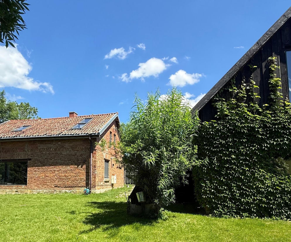 Ceglany dom i czarna stodoła na tle nieba. O renowacji mazurskiego siedliska przeczytasz na Muratordom.