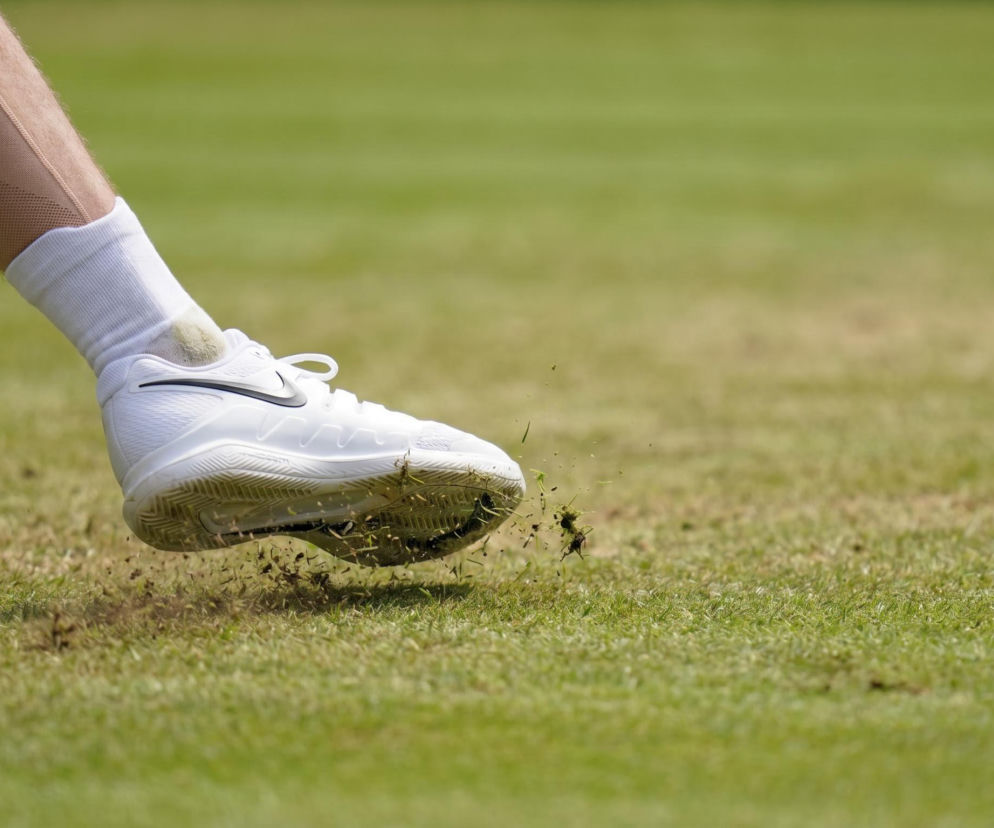 Noga tenisisty w białym bucie sportowym Nike, wyrzucająca trawę podczas ruchu na zielonym korcie, obok leży żółta piłka tenisowa. Więcej o meczu Igi Świątek przeczytasz na naszym portalu.