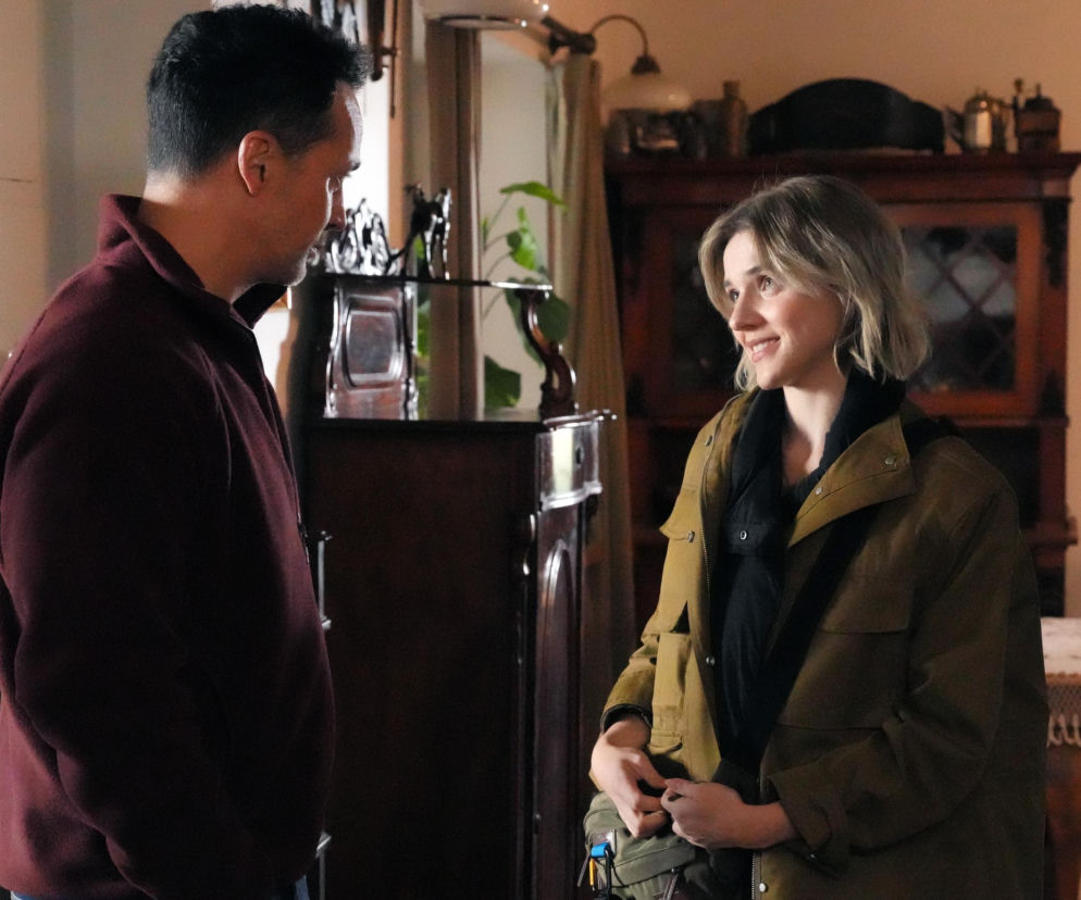 Aktor Rafał Cieszyński jako Mariusz i Oliwia Drożdżyk jako Janka rozmawiają w pomieszczeniu, na zdjęciu z serialu Barwy szczęścia dostępnym na portalu Super Seriale. Mariusz w bordowej bluzie, Janka w zielonej kurtce, patrzą na siebie z uśmiechem, w tle meble i firany.