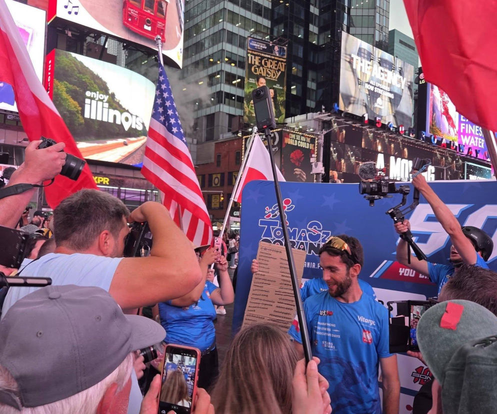 Tomasz Sobania, polski biegacz, podczas powitania na Times Square w Nowym Jorku, otoczony kibicami z polskimi i amerykańskimi flagami. Tłum świętuje jego wyczyn – przebiegnięcie 50 maratonów w 50 stanach USA w 49 dni, o czym więcej przeczytasz na naszym portalu.