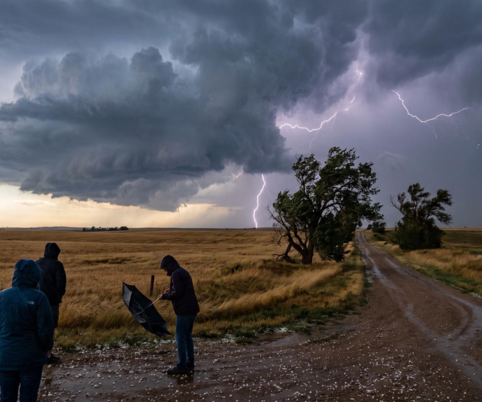 Ludzie patrzący na burzę i pioruny nad polami. O ostrzeżeniach meteorologicznych IMGW przeczytasz w serwisie Eska.