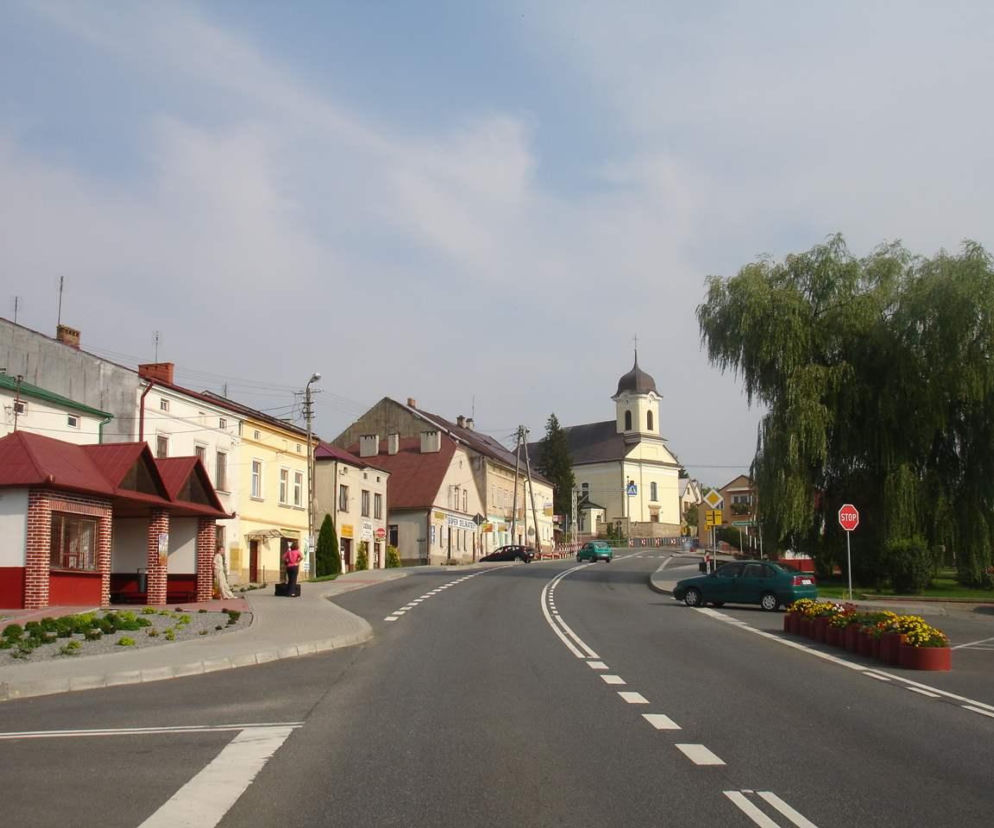 Rynek w Brzostku z widokiem na kamienice, kościół i duże zielone drzewa. O rewitalizacji miasta przeczytasz na Architektura.