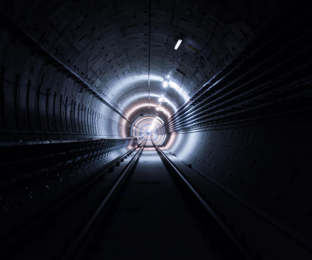 Tunel metra w budowie, z wyraźnie widocznymi torami i systemem oświetlenia liniowego, symbolizujący rozwój nowoczesnej infrastruktury transportowej. Więcej o planach na metro w Krakowie przeczytasz na Architektura Murator Plus.