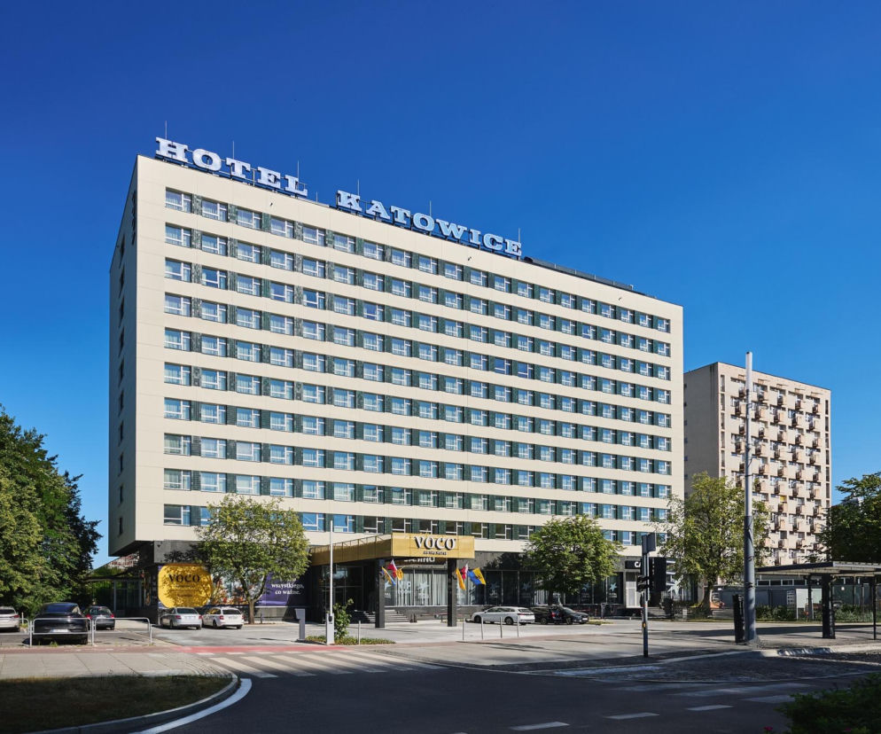 Jasny, modernistyczny Hotel Katowice voco z granatowym neonem na dachu, otoczony zielenią i drogami, symbolizuje udaną modernizację obiektu. O tej transformacji przeczytasz więcej na portalu Architektura Murator Plus.