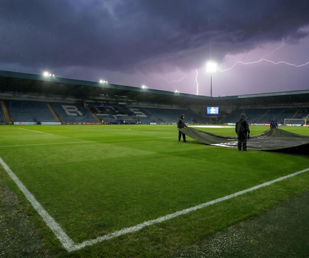 Stadion piłkarski podczas gwałtownej burzy z piorunami, z personelem rozkładającym plandekę na boisku, co ilustruje przymusowe przerwanie meczu. Na naszym portalu przeczytasz o przebiegu spotkania Francja-Irak na MŚ 2026 i wysokich cenach biletów.