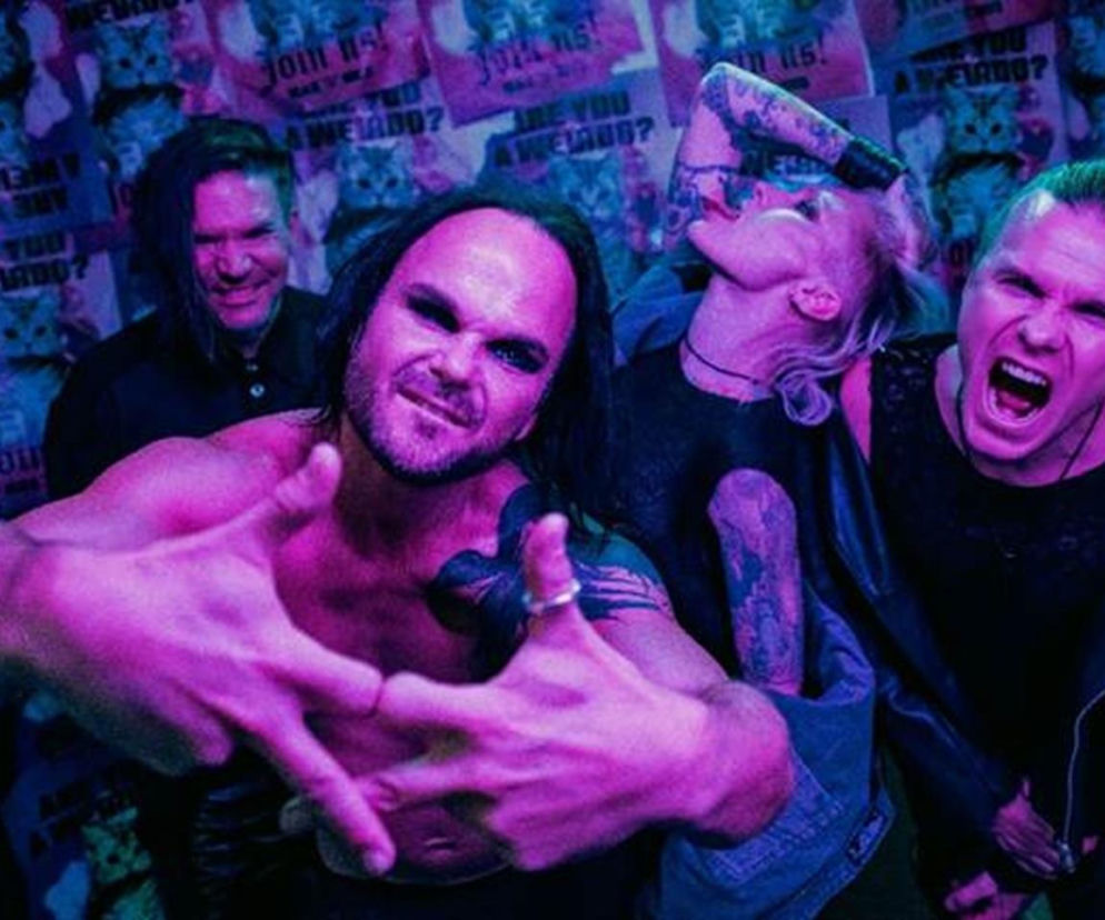 Członkowie zespołu The Rasmus w ujęciu z bliska, oświetleni fioletowo-niebieskim światłem scenicznym, z frontmanem Laurim Ylönenem na pierwszym planie, wykonującym gest dłońmi. Zdjęcie oddaje dynamiczną energię zespołu, o którego koncertach w Polsce przeczytasz na naszym portalu.