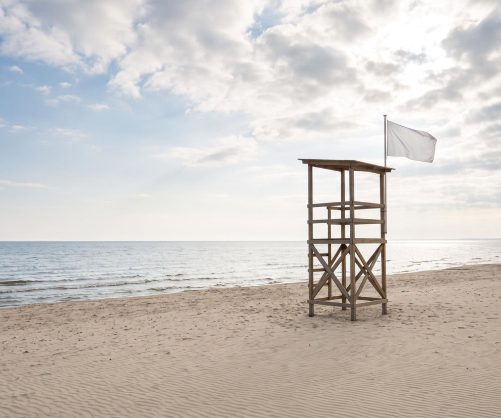 Drewniana wieża ratownicza z białą flagą na plaży w Mrzeżynie. O otwartych kąpieliskach przeczytasz na SE Szczecin.