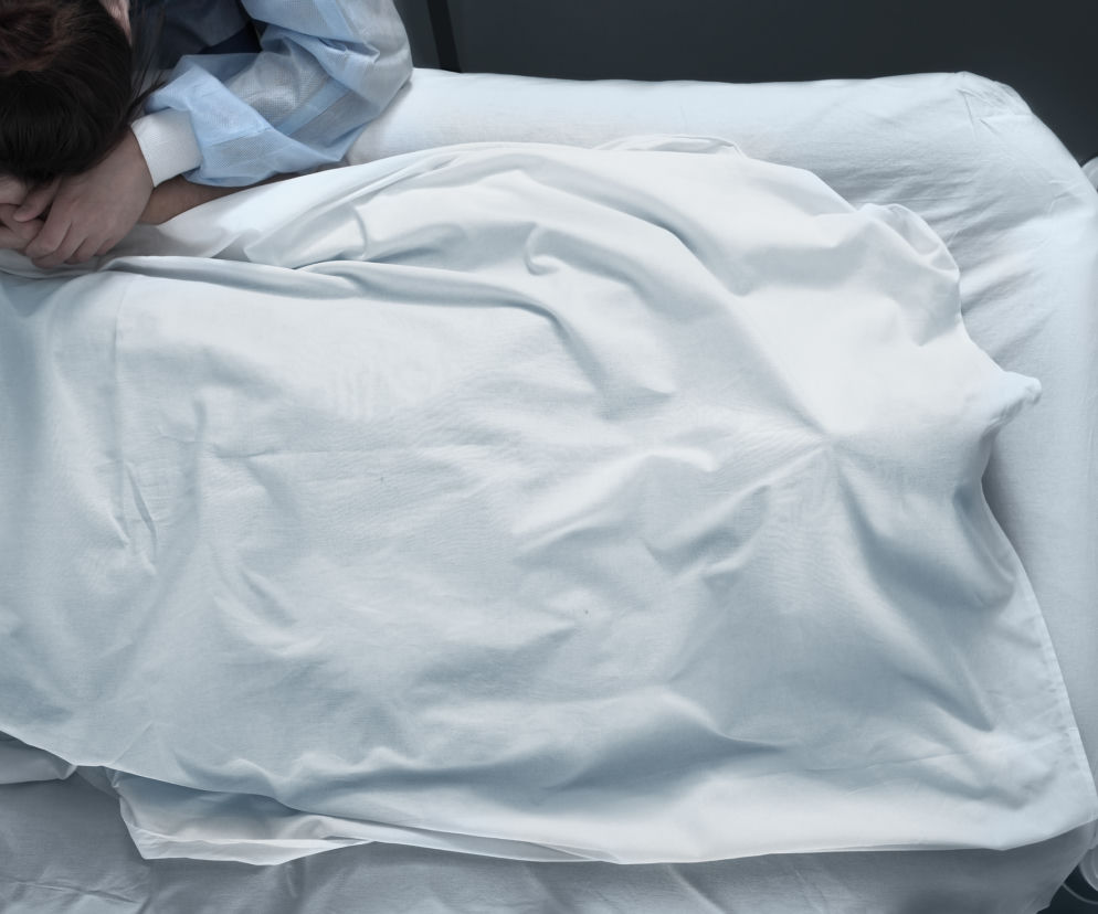 zbliżenie na szpitalne łóżko, nad którym pochyla się kobieta