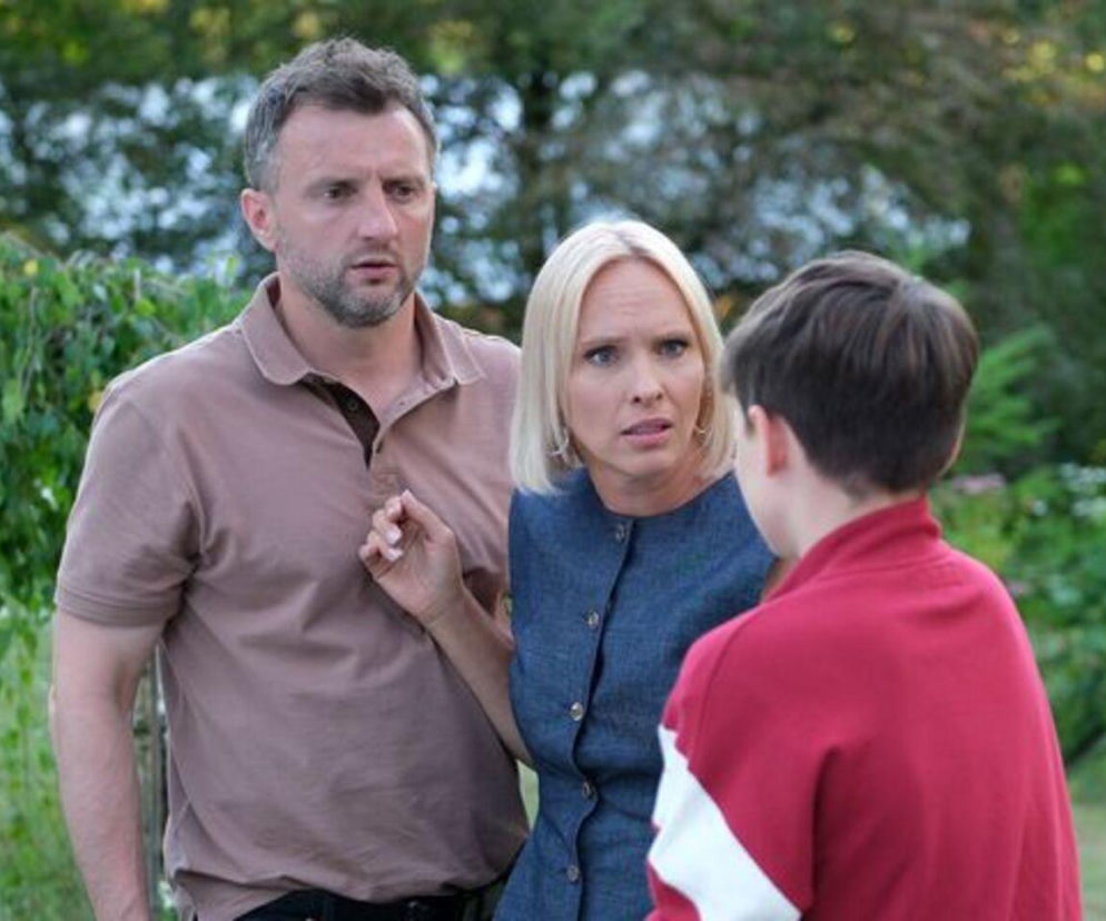 Dorota (Iwona Rejzner) i Bartek (Arkadiusz Smoleński) Lisieccy zaniepokojeni rozmawiają z Frankiem (Jarosław Śmigielski) w ogrodzie siedliska w Grabinie, tłem są zielone krzewy. Zdjęcie ilustruje trudną sytuację z serialu M jak miłość, o której można przeczytać na Super Seriale.