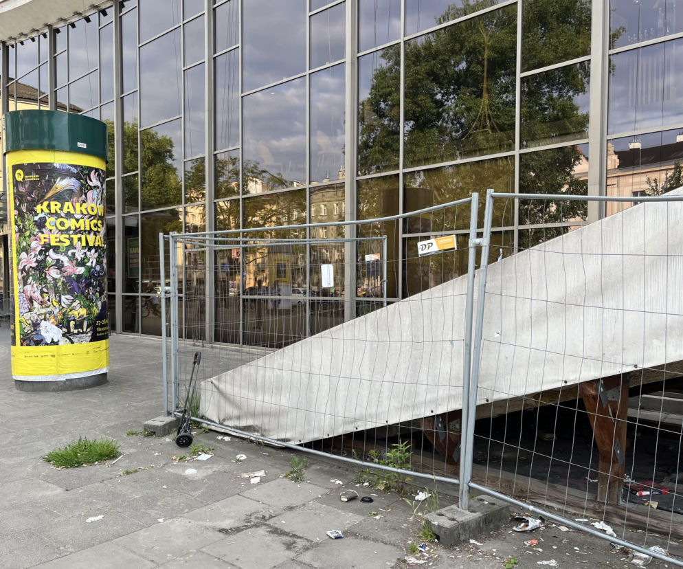 Schody esplanady między Kinem Kijów a Hotelem Cracovia w Krakowie, zasłonięte brudnym brezentem i ogrodzeniem budowlanym, otoczone śmieciami. Obok widoczna reklama „Krakow Comics Festival”. Artykuł o tym problemie na Architektura Murator Plus.