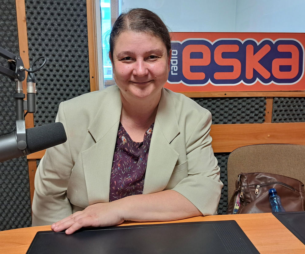 Katarzyna Bochenek, uśmiechnięta kobieta w beżowej marynarce i wzorzystej bluzce, siedzi przy mikrofonie radiowym, prezentując nocne zwiedzanie Muzeum Drogownictwa w Szczucinie. Więcej o wydarzeniu na naszym portalu.