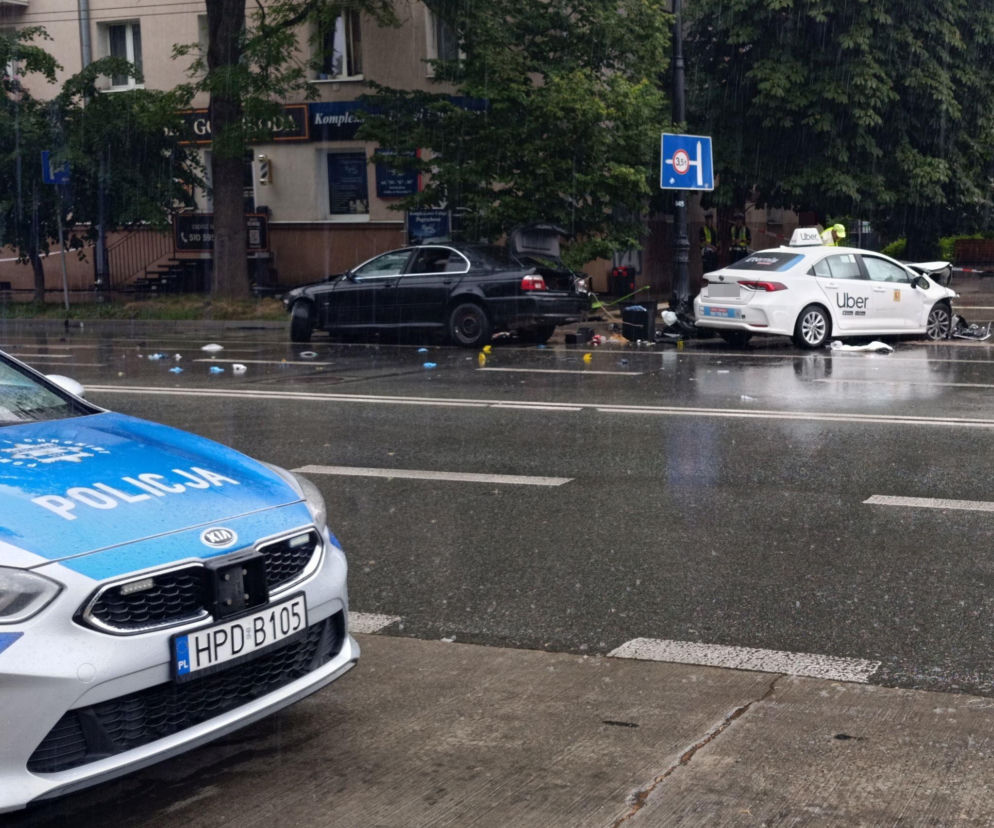 Radiowóz policyjny na pierwszym planie, a w tle zniszczone samochody – czarne BMW i biała Toyota Ubera, po śmiertelnym wypadku na ul. Lipowej w Lublinie. Wokół pojazdów leżą odłamki, a na mokrej jezdni widać policyjne znaczniki. Więcej o tragedii przeczytasz na naszym portalu.