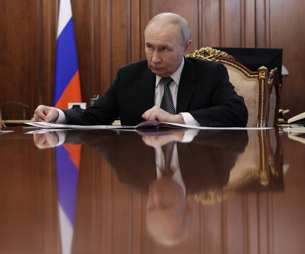 Władimir Putin siedzi przy dużym stole konferencyjnym na tle rosyjskiej flagi. O wizycie dyplomacji Watykanu przeczytasz na SE.