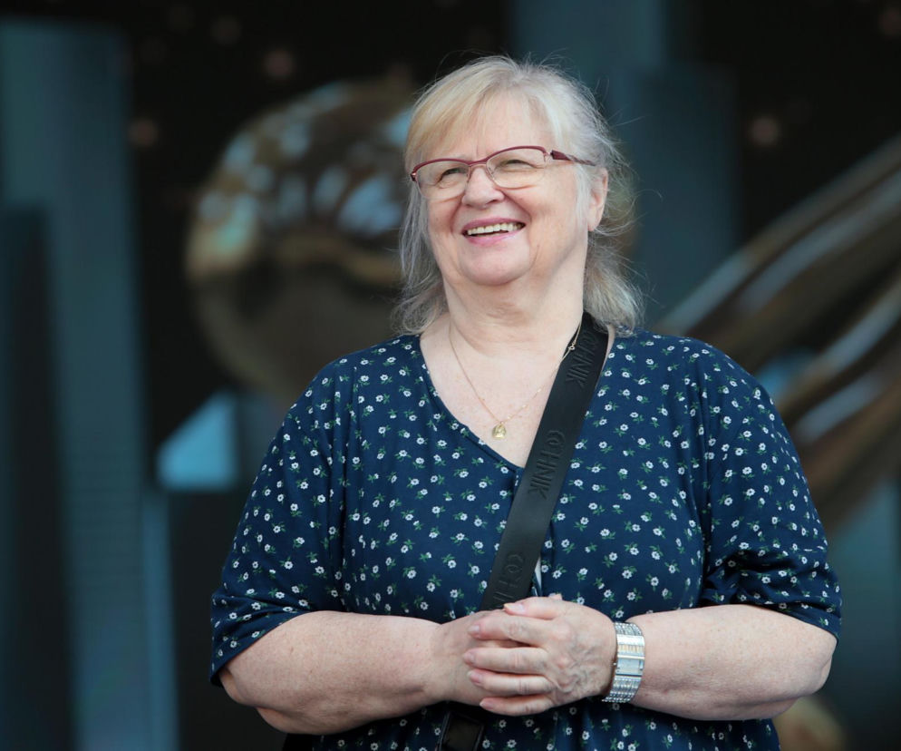 Stanisława Celińska, polska aktorka i wokalistka, uśmiecha się na scenie, ubrana w ciemnoniebieską sukienkę w białe kwiatki, z okularami na nosie. Zdjęcie przedstawia artystkę w pozytywnym świetle, mimo informacji o jej zmaganiach zdrowotnych, o których więcej można przeczytać na Poradnik Zdrowie.