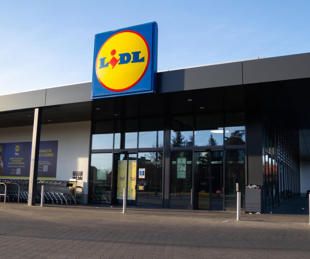 Budynek sklepu Lidl z widocznym logotypem sieci na tle błękitnego nieba. Przed wejściem do marketu stoją rzędy wózków sklepowych oraz banery reklamowe akcji Lidl Plus. Informacje o promocjach na sprzęty kuchenne znajdziesz na Super Biznes.