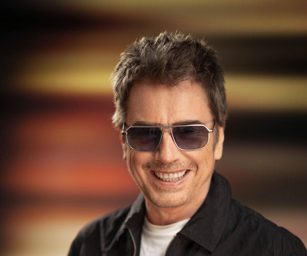 Uśmiechnięty Jean-Michel Jarre w ciemnych okularach przeciwsłonecznych. O reedycji Oxygène przeczytasz na EskaRock.