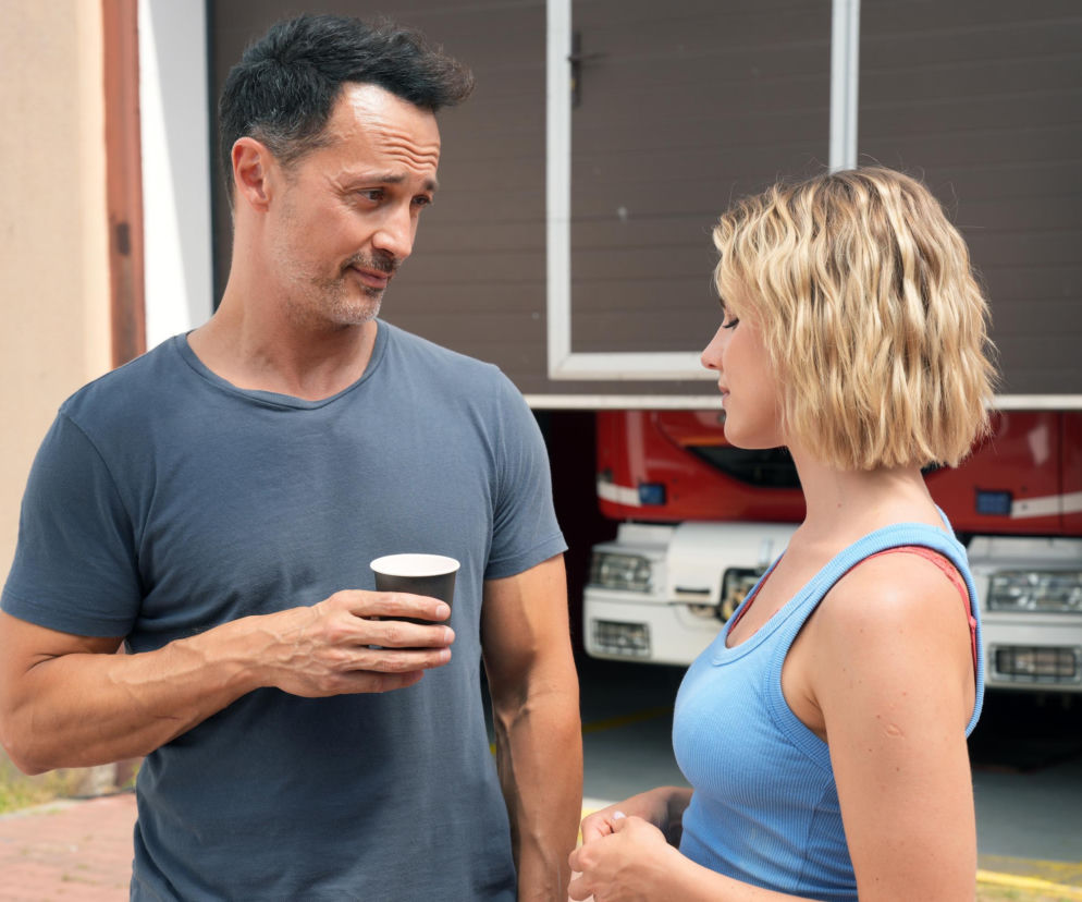 Aktor Rafał Cieszyński jako Mariusz, trzymający kubek, patrzy na Oliwię Drożdżyk, która gra Jankę, w scenie z Barw szczęścia. Fotografia ilustruje moment, gdy Mariusz odtrąca Jankę, zachowując pamięć o Kasi, co jest istotne dla fabuły serialu dostępnego na Super Seriale.