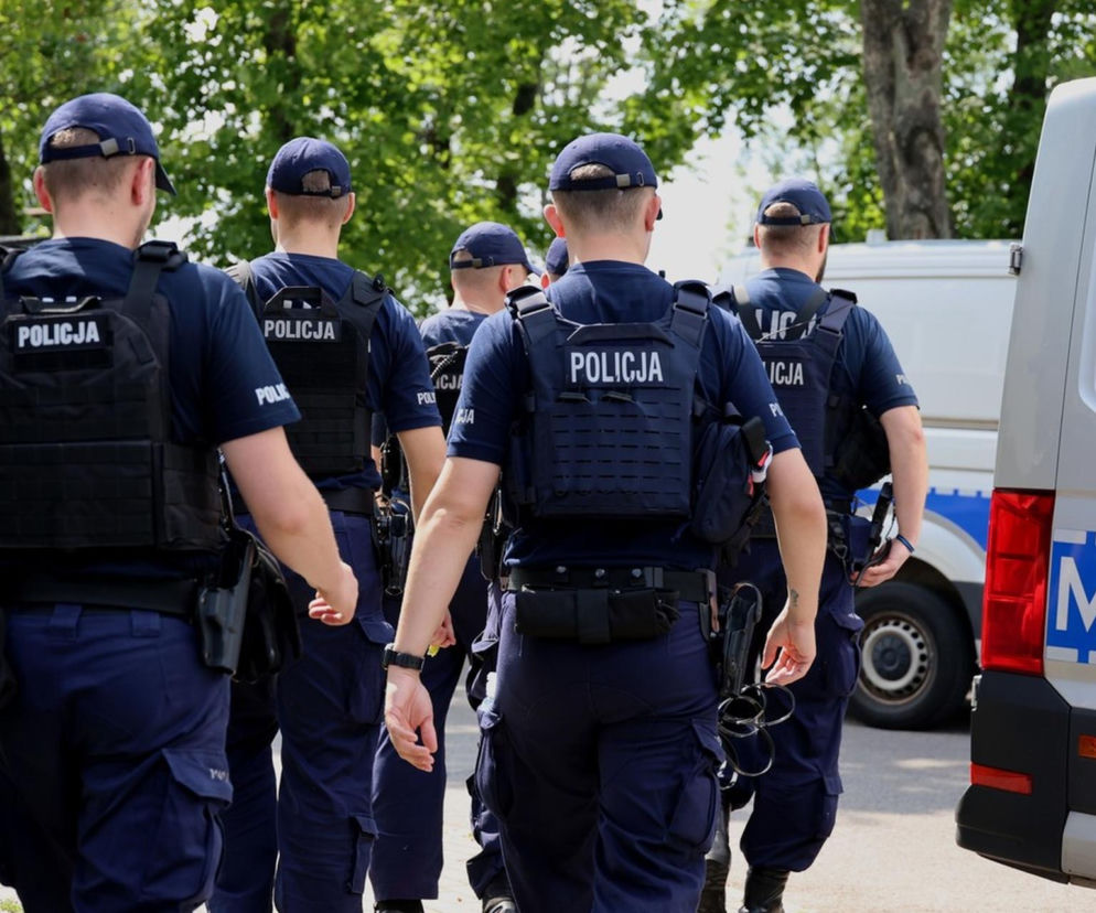 Policjanci w kamizelkach taktycznych idą obok radiowozów. O kontrolach przy szkołach przeczytasz na SE Białystok.