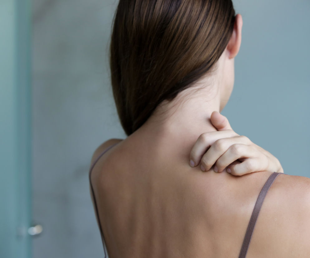 Kobieta dotyka karku, co symbolizuje dolegliwości bólowe lub zgrubienie, takie jak wdowi garb lub bawoli kark, będące sygnałem poważnych zaburzeń hormonalnych. Więcej o ich rozróżnianiu oraz leczeniu przeczytasz na portalu Poradnik Zdrowie.