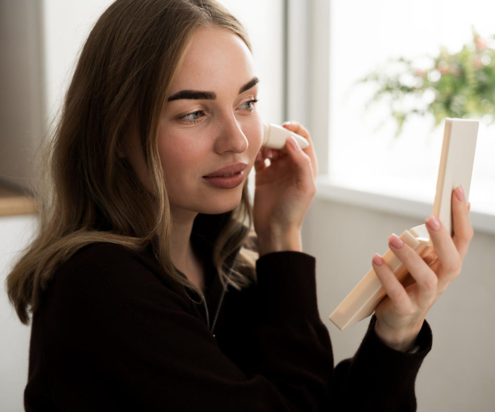 Kobieta wykonująca latte makeup przed lusterkiem. O trendach w makijażu przeczytasz na PZ Uroda.
