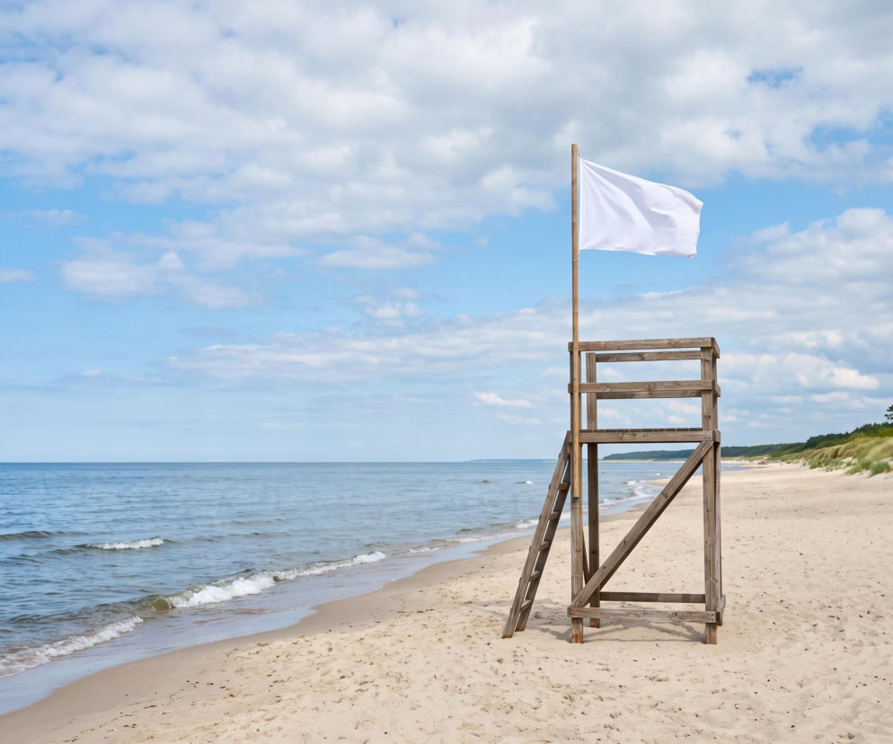 Drewniana wieża ratownicza na piaszczystej plaży z białą flagą. O warunkach kąpieli w Pobierowie przeczytasz na SE Szczecin.