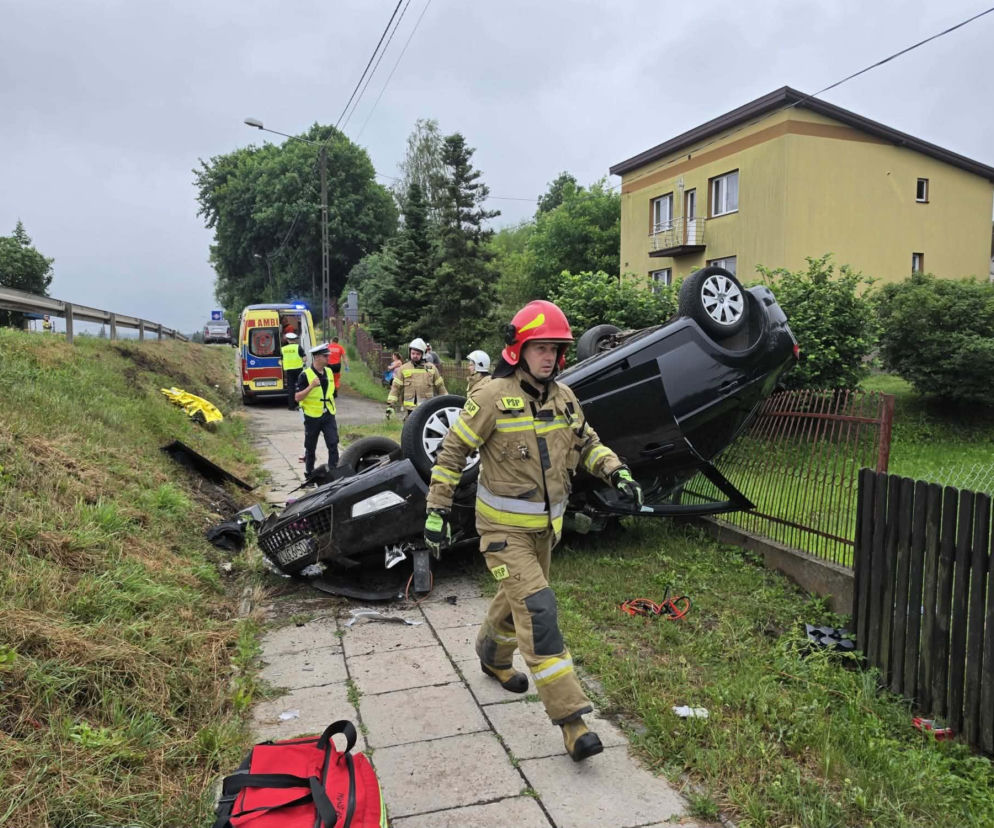 Strażak idzie chodnikiem obok czarnego auta leżącego na dachu. O wypadku w Stykowie przeczytasz na Eska Starachowice.