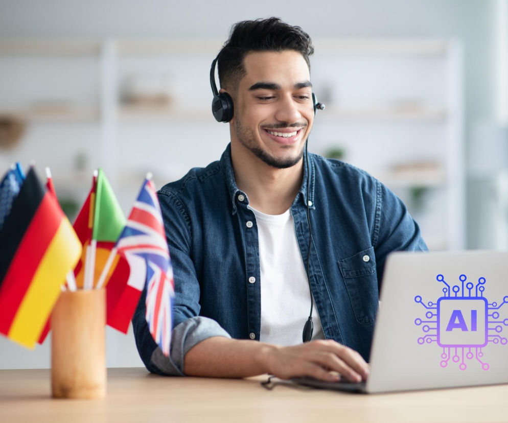 Młody, uśmiechnięty mężczyzna w słuchawkach z mikrofonem, w denimowej koszuli, pracuje na laptopie z naklejką symbolizującą sztuczną inteligencję. Obok niego miniaturowe flagi różnych krajów, co odzwierciedla kontekst nauki języków obcych. Więcej o roli AI w edukacji językowej przeczytasz na Super Biznes.