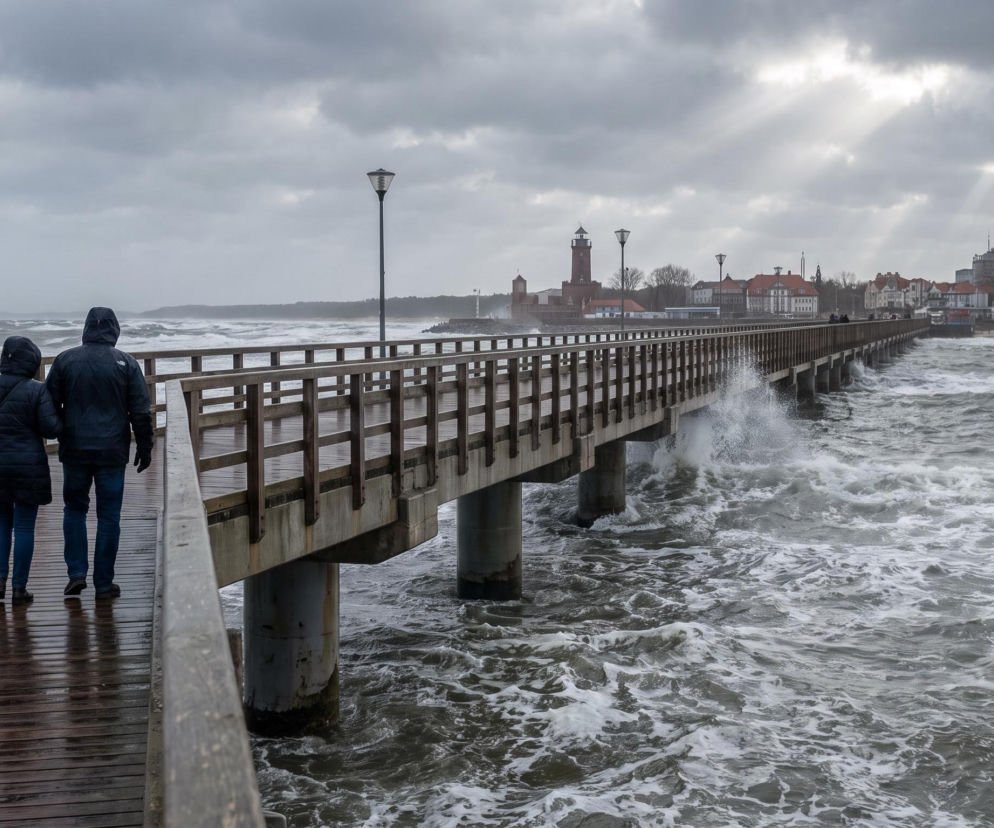Dwie osoby spacerujące po molo w Kołobrzegu podczas sztormu. O otwarciu mola po wichurach przeczytasz w Eska.