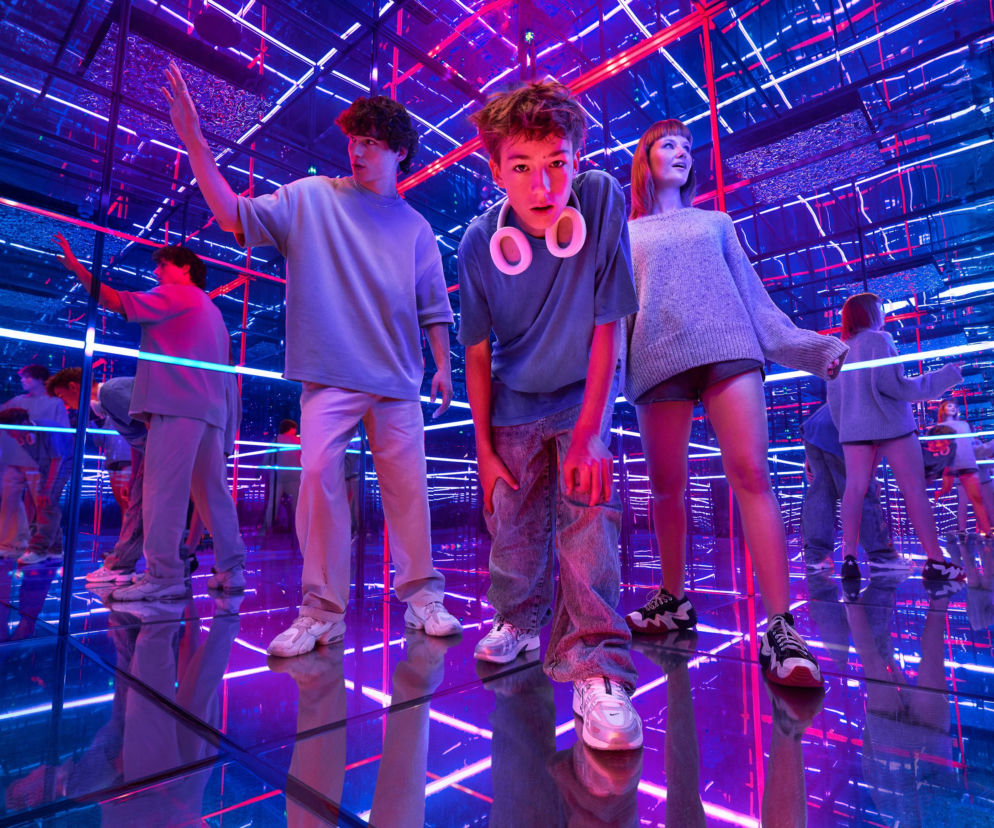 Trójka młodych osób w lustrzanej instalacji z niebieskimi i różowymi neonami w Melt Museum, o którym przeczytasz na SE.