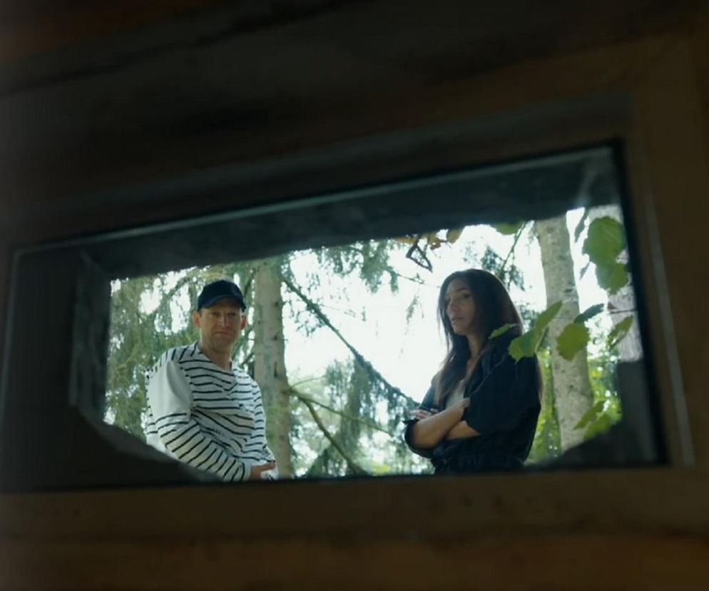 Michał Rolnicki jako Łukasz Sadowski i Orina Krajewska jako Celina Brońska stojący w lesie, widziani z wnętrza ciemnego pomieszczenia przez małe okno, co ilustruje powrót Łukasza do miejsca uwięzienia w Barwach szczęścia. Więcej o serialu na Super Seriale.