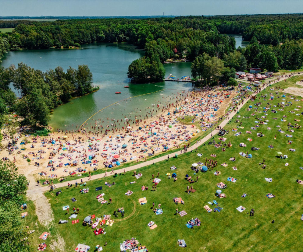 Tłumy ludzi na piaszczystej plaży i zielonej trawie nad jeziorem. O śląskich kąpieliskach przeczytasz na SE.