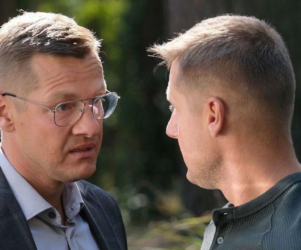 Mężczyźni: Rafał Mroczek jako Paweł Zduński i Marcin Mroczek jako Piotrek Zduński z serialu M jak miłość podczas poważnej rozmowy, na tle zielonego, rozmytego krajobrazu. Na Super Seriale znajdziesz więcej szczegółów o tym odcinku.