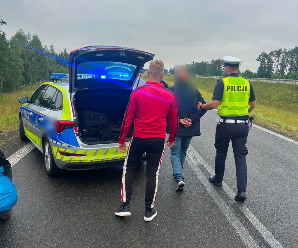 Policjant prowadzi zakutego w kajdanki mężczyznę do radiowozu. O zatrzymaniu pijanego kierowcy przeczytasz na Radioplus.