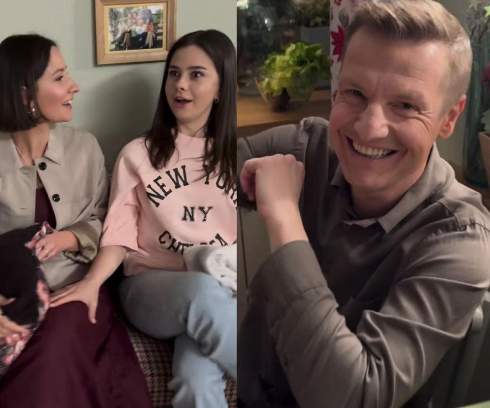 Rafał Mroczek jako Paweł Zduński uśmiecha się radośnie, siedząc przy stole. Obok, dwie kobiety rozmawiają w tle, prawdopodobnie Paulina Chruściel jako Judyta i Karina Woźniak jako Basia. Aktor potwierdza pozytywną przemianę Pawła w serialu, o czym przeczytasz na Super Seriale.