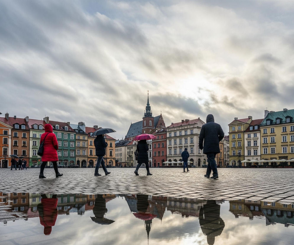 Na pierwszym planie, sześć osób idzie po mokrym, brukowanym placu; trzy z nich niosą otwarte parasole. Po lewej, osoba w czarnej kurtce i dżinsach trzyma czarny parasol, a obok niej idzie osoba w czerwonym płaszczu z czarną torbą na ramieniu. Kolejno, osoba w ciemnym płaszczu z czarnym parasolem, osoba w ciemnym płaszczu z różowym parasolem, i znowu osoba w ciemnym płaszczu, a po prawej osoba w czarnej kurtce. Na powierzchni placu odbijają się postacie, parasole i fasady budynków.

Tło wypełnia rząd kolorowych kamienic, z których każda ma kilka okien i dachów w odcieniach czerwieni, zieleni i brązu. Pomiędzy kamienicami wznosi się ciemny kościół z wysoką wieżą zakończoną iglicą, na której szczycie znajduje się krzyż. Nad miastem rozciąga się zachmurzone niebo, przez które przebija się jasne światło słoneczne, tworząc świetlistą poświatę w centrum kadru.