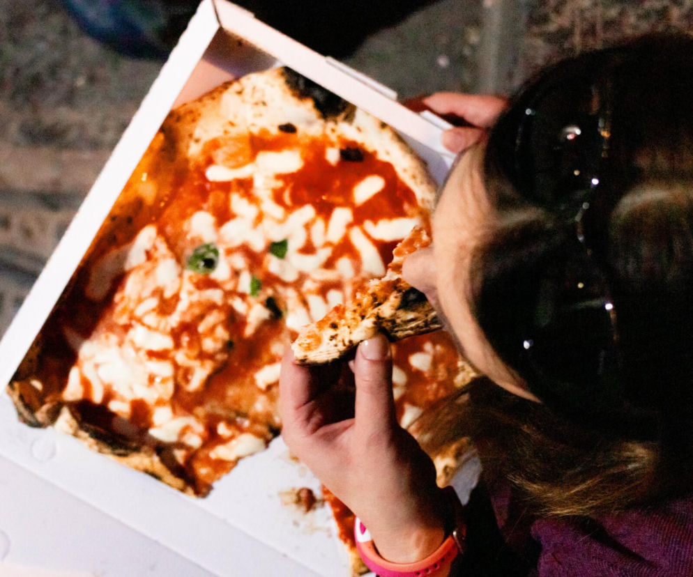 Osoba jedząca kawałek pizzy z pudełka. O rosnącym zadłużeniu młodych Polaków na jedzenie przeczytasz na SE Superbiz.
