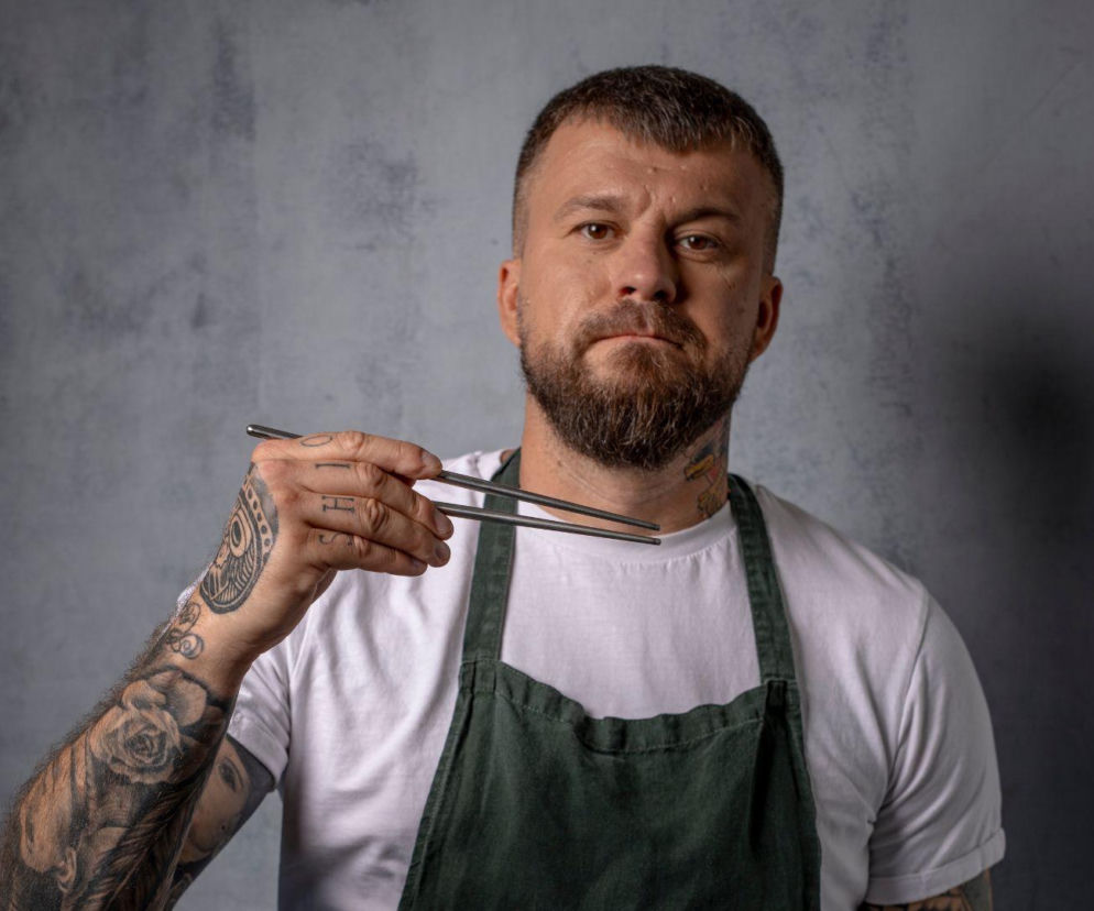 Bartosz „Snecz” Dębski, szef kuchni i twórca street foodowego projektu SPOKO SZAMA, z powagą trzyma metalowe pałeczki, prezentując styl Carmycore. Ta estetyka, łącząca japoński denim i workwear, zyskuje na popularności, o czym przeczytasz na naszym portalu.