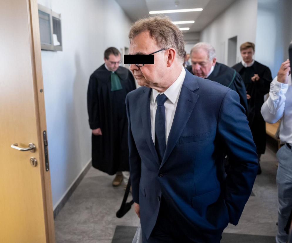 Profesor Dariusz S. w ciemnym garniturze i krawacie, z zamazanymi oczami, opuszcza salę sądową w Poznaniu, otoczony przez prawników w togach i dziennikarzy z kamerą. To właśnie o nim i jego procesie przeczytasz więcej na naszym portalu.