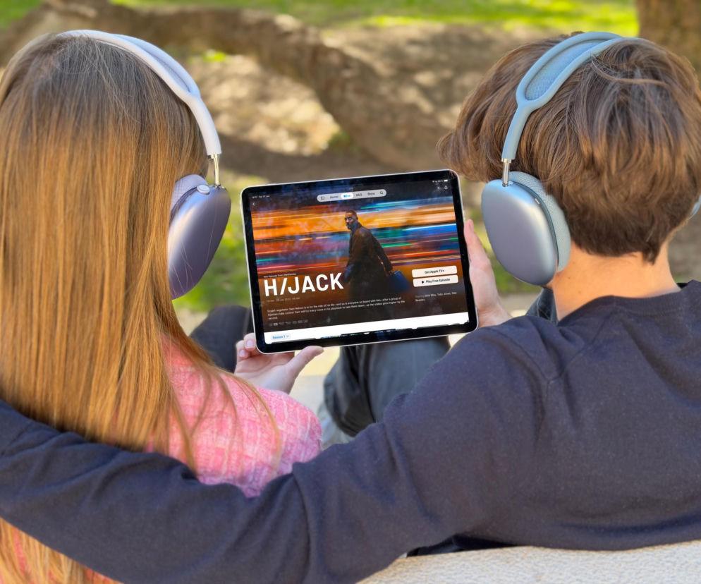 Para oglądająca film Hijack na tablecie, używając słuchawek Apple AirPods Max w kolorze niebieskim i srebrnym. Model ukazuje immersję dźwięku, o której można przeczytać więcej na naszym portalu. Słuchawki zapewniają odcięcie od świata i komfort.