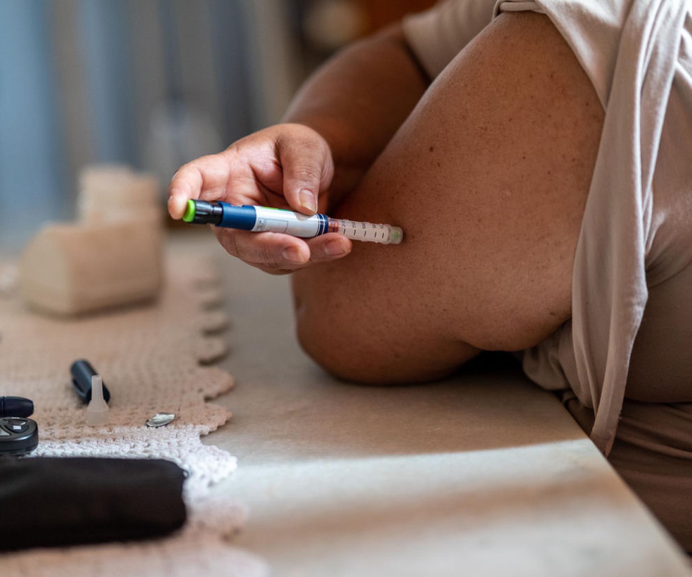 Osoba ze stanem przedcukrzycowym w jasnej koszulce wstrzykująca insulinę w ramię przy użyciu pena insulinowego, obok leży glukometr, co jest ważne w kontekście witaminy D i cukrzycy, o czym przeczytasz na Poradnik Zdrowie.